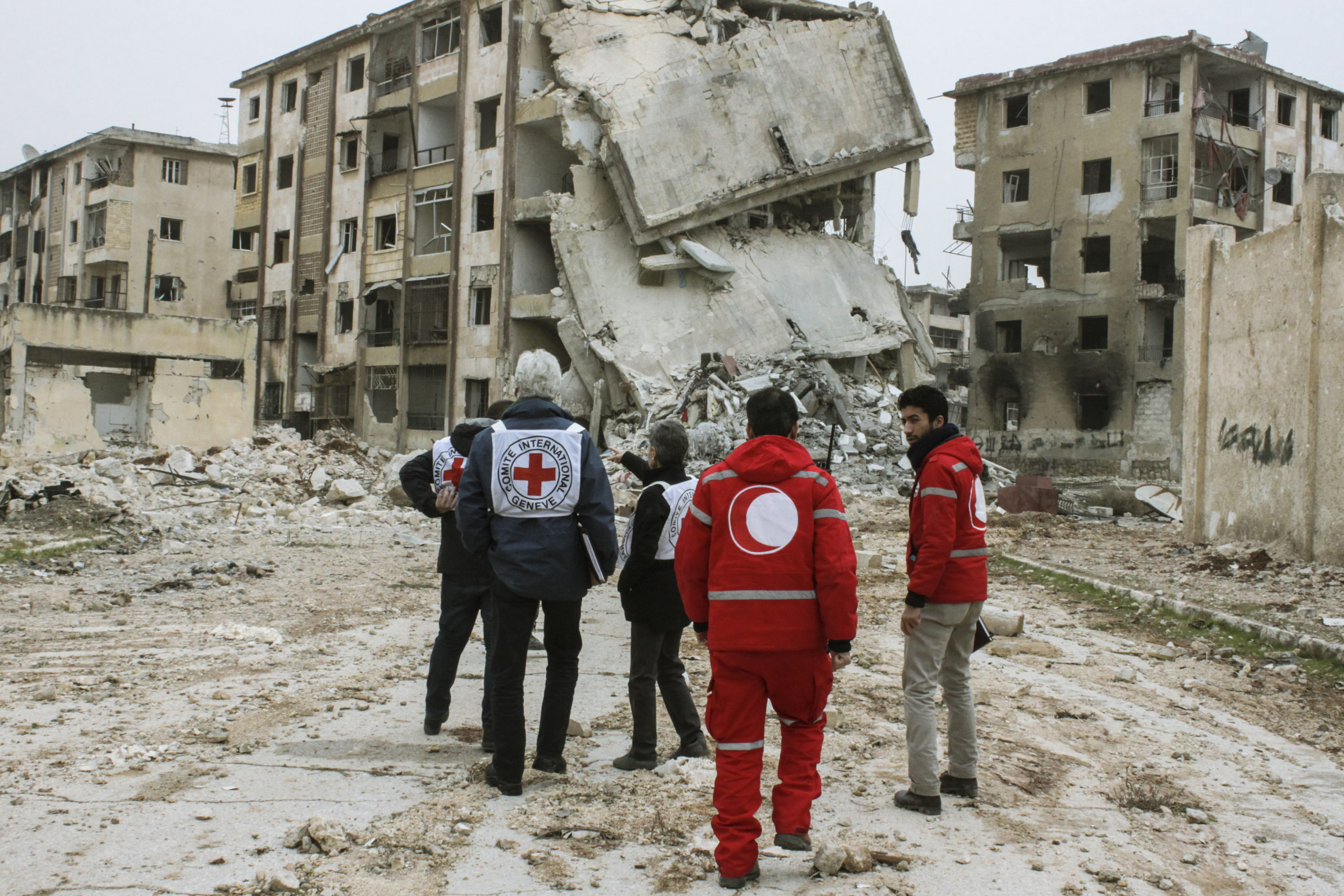 ICRC and Red Crescent personnel are walking towards a destroyed building in Aleppo, Syria.