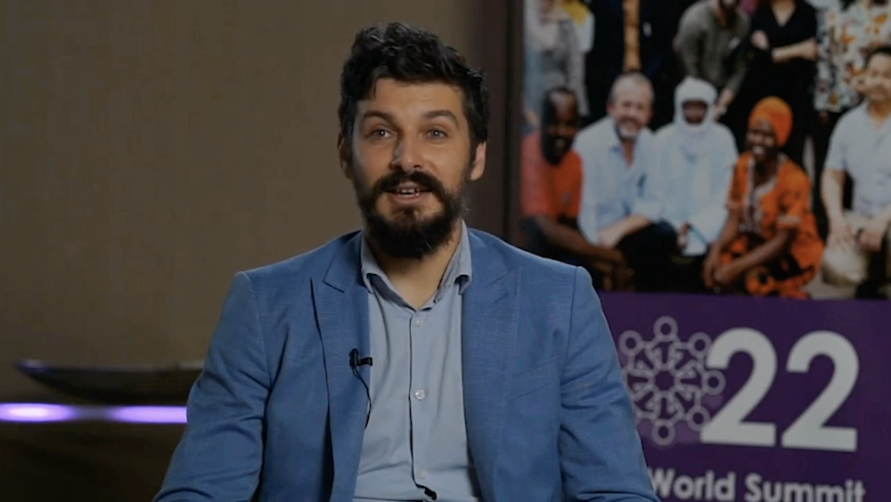 Andrii Kruglashov is sitting on a chair wearing a suit and a microphone on his lapel. He is being interviewed about his experience battling misinformation in Ukraine.